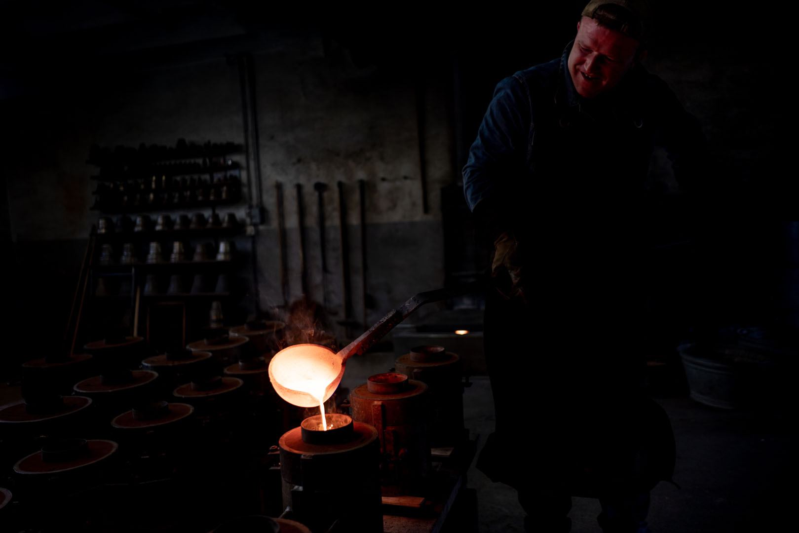 Dans la pénombre de la Fonderie, une louche de bronze en fusion