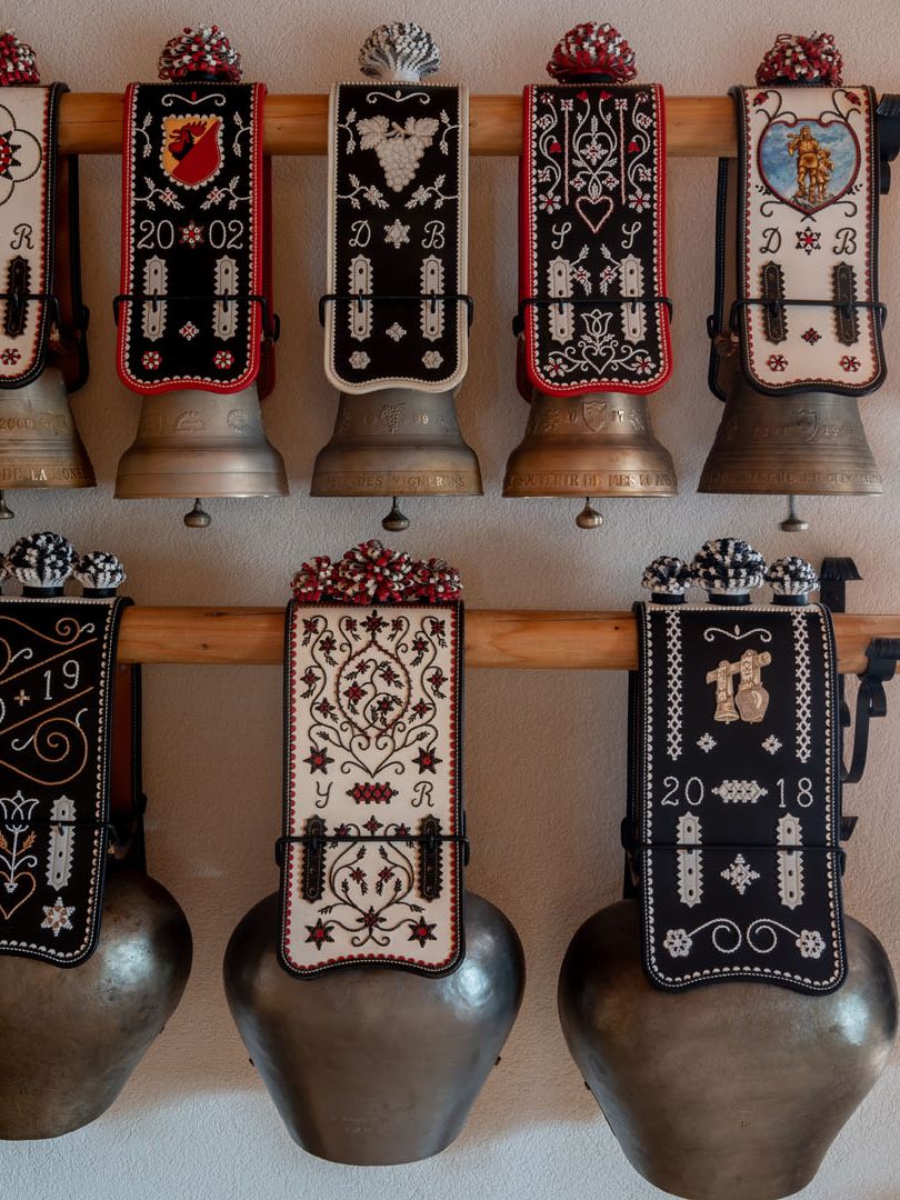 Des sonnailles et leurs courroies brodées alignées au mur de l'atelier